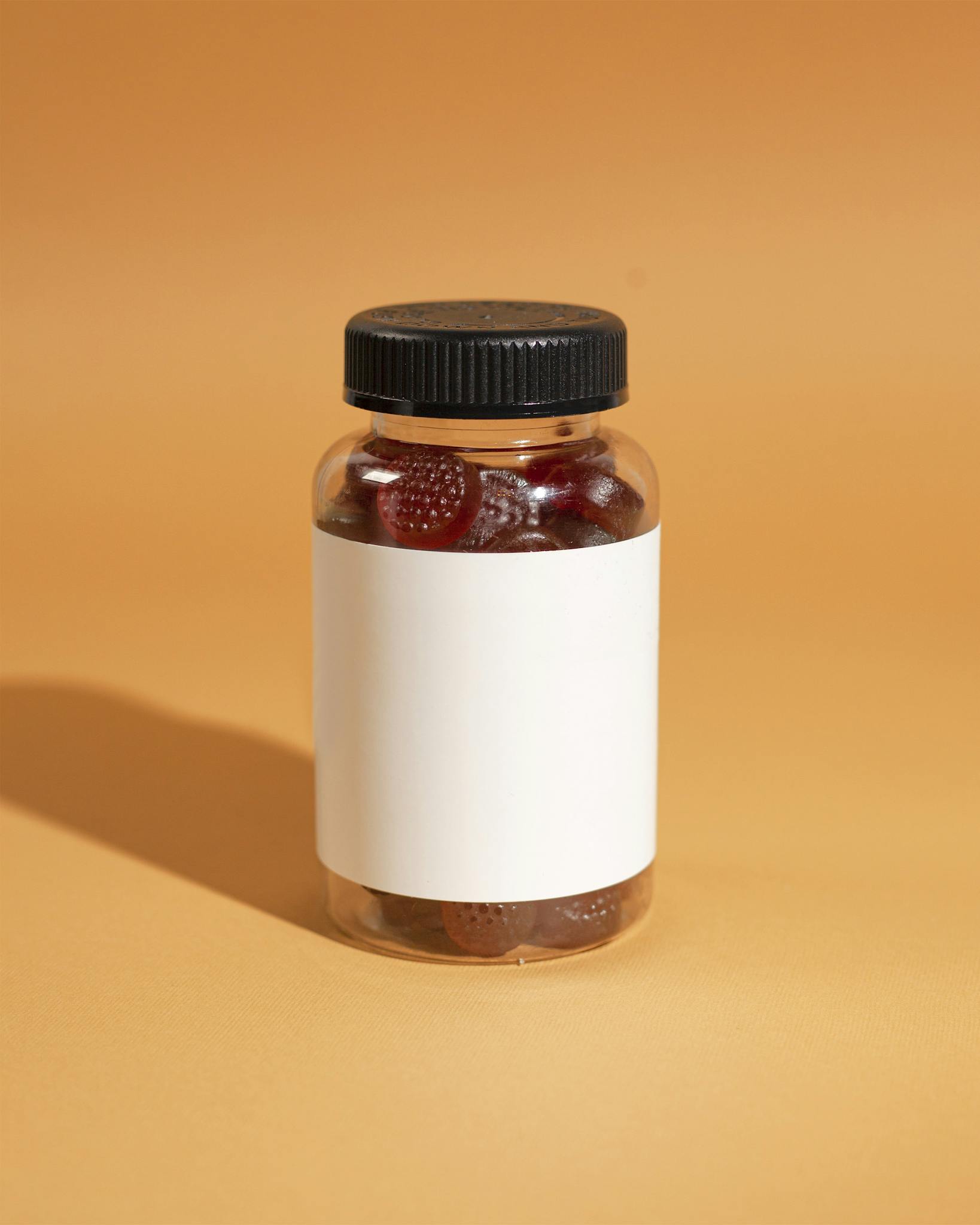 A clear bottle filled with gummy vitamins on an orange background, ideal for health and wellness themes.